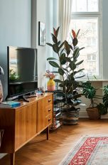 Eine Person steht in einem Wohnzimmer und telefoniert. Auf einer TV-Bank ist ein Fernseher zu sehen.