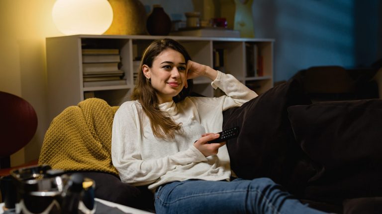 Stromverbrauch beim Fernseher Eine Person sitzt auf einem Sofa und hält eine Fernbedienung in der Hand.