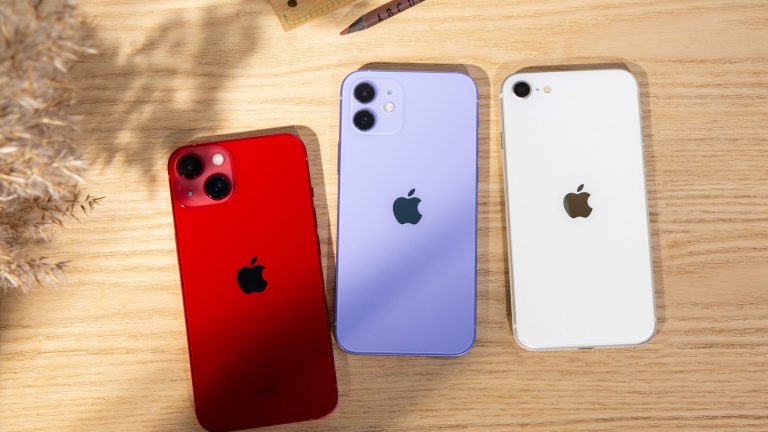 Auf einem Tisch liegen mit der Rückseite nach oben iPhone 13, iPhone 12 und iPhone SE.