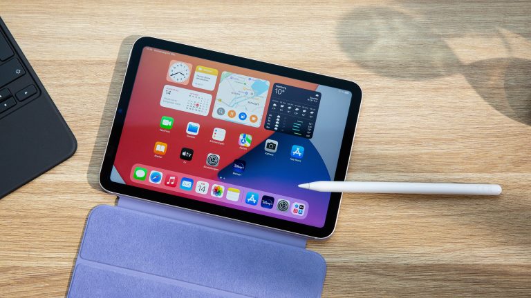 Apple iPad mini Ein iPad mini samt aufgeklapptem Smart Folio und ein Apple Pencil 2 liegen auf einem Holztisch. Auf dem iPad mini ist der Homescreen mit den Standard-Apps von Apple zu sehen.