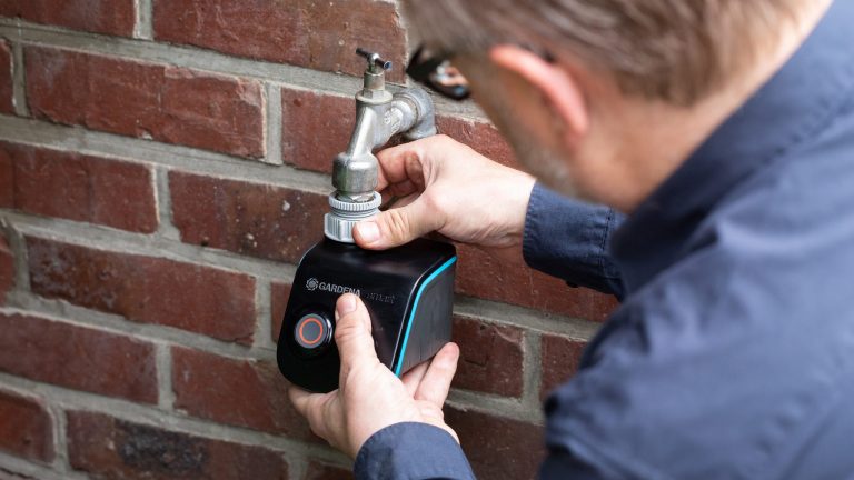 Eine Person bringt einen Bewässerungscomputer an einem Wasserhahn an.