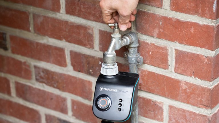 Gardena smart Water Control Eine Person öffnet den Wasserhahn, an dem ein Bewässerungscomputer hängt.