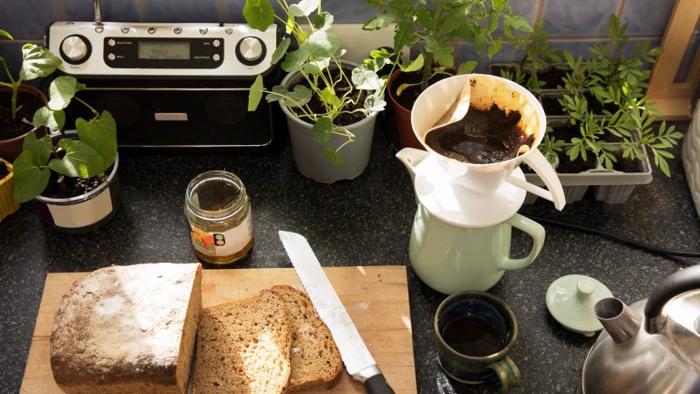 DAB+ Ein DAB+-Radio steht in einer Küche auf der Arbeitsplatte, davor ein Holzbrett mit geschnittenem Brot, ein Glas Marmelade, eine Kaffeekanne mit Filter und eine Tasse.