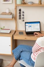 Eine Person sitzt vor einem Laptop, auf einem Regal neben ihr steht eine FritzBox.