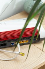Eine FritzBox steht mit der Rückseite zur Kamera auf einem Regal. Es sind zwei LAN-Kabel zu sehen.
