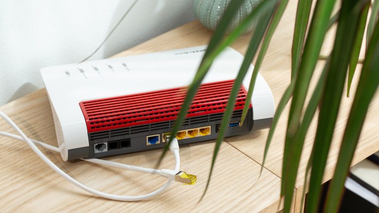 Eine FritzBox steht mit der Rückseite zur Kamera auf einem Regal. Es sind zwei LAN-Kabel zu sehen.