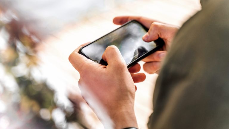Gaming-Smartphones Eine Person hält ein Smartphone quer in beiden Händen und bedient darauf ein Videospiel.