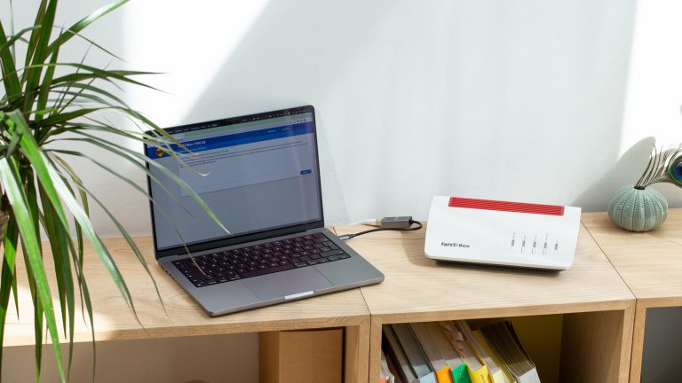 Heimnetzwerk einrichten Laptop und FritzBox stehen auf einem Regal nebeneinander.