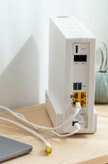 Neben einem Laptop steht ein Router, aus dem ein LAN-Kabel herausführt.