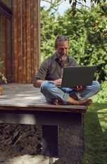 Eine Person sitzt mit einem Laptop auf einer Terrasse.