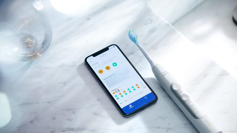 Elektrische Zahnbürsten Eine Schallzahnbürste der Philips-Sonicare-Reihe liegt neben einem Smartphone auf einem Badezimmerschrank.