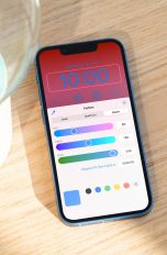 iOS 16 Public Beta Auf einer Holzkiste neben einer Lampe liegt ein iPhone 13 Pro Max, auf dem gerade die Farbeinstellungen des neuen Sperrbildschirms zu sehen sind.