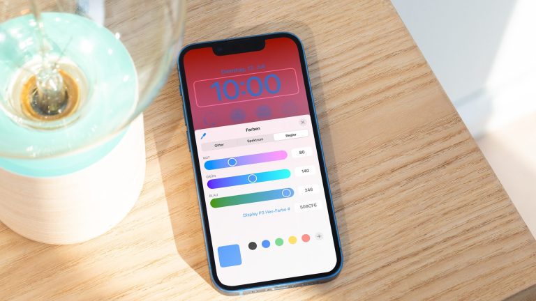 Auf einer Holzkiste neben einer Lampe liegt ein iPhone 13 Pro Max, auf dem gerade die Farbeinstellungen des neuen Sperrbildschirms zu sehen sind.