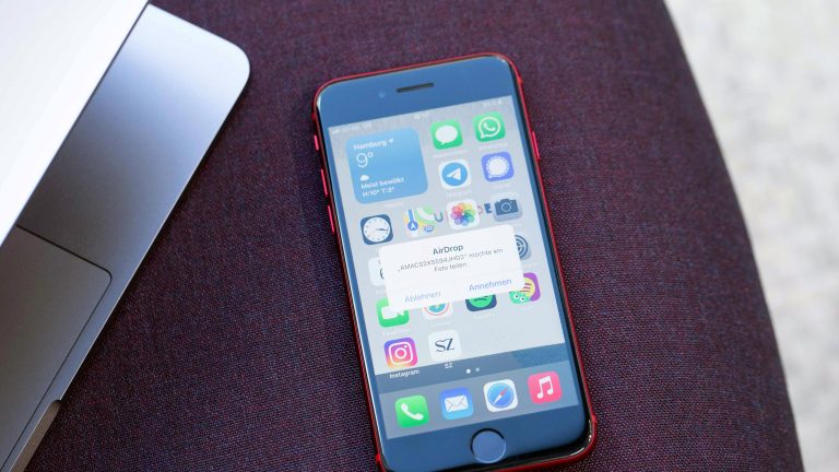 Ein iPhone SE liegt neben einem MacBook. Auf dem Display des Smartphones ist eine AirDrop-Meldung zu sehen.