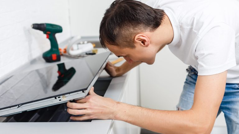 Induktionsfeld anschließen Eine Person fasst ein Induktionskochfeld in eine Arbeitsplatte ein Im Hintergrund ist etwas Werkzeug zu sehen.