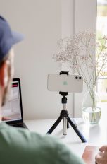 Eine Person sitzt vor einem MacBook und schaut in ein iPhone, das daneben als Webcam dient.