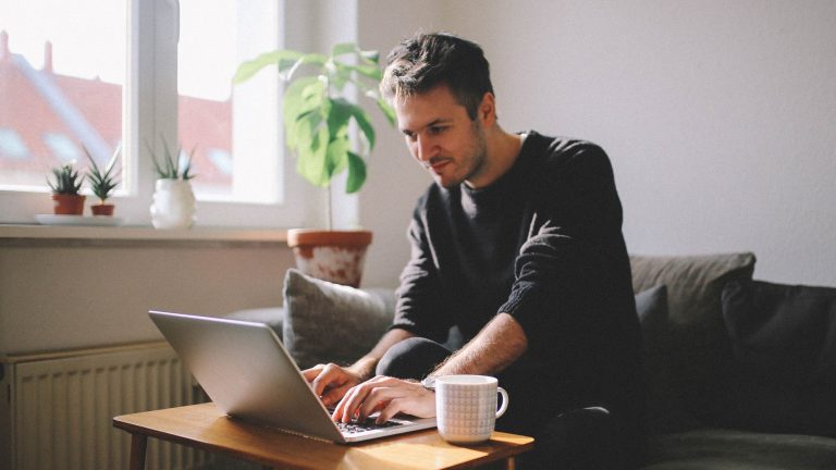 Eine Person sitzt auf einem Sofa und tippt auf der Tastatur eines Laptops.