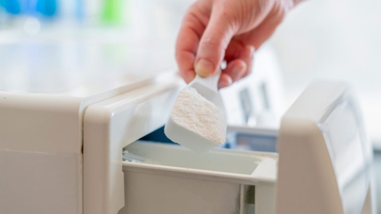 Waschmaschine entkalken Eine Person gibt etwas Waschmittel in das entsprechende Fach einer Waschmaschine.