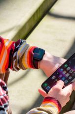 Eine Person trägt eine Apple Watch am Handgelenk und hält in der rechten Hand ein iPhone.