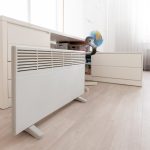 Eine Elektroheizung steht vor einem Schreibtisch am Boden.