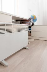 Eine Elektroheizung steht vor einem Schreibtisch am Boden.