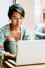 Eine Person sitzt in einem Café und bedient einen Laptop.