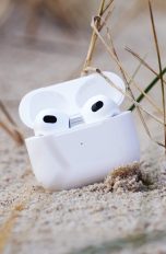 AirPods der dritten Generation in ihrem Case liegen auf einer Sandbank.