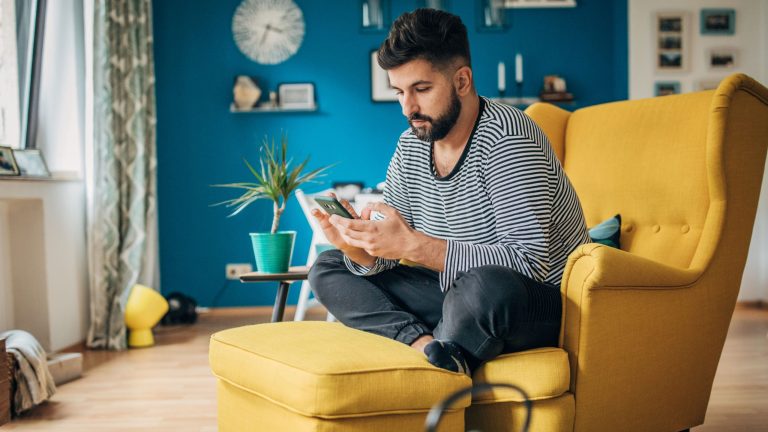 Eine Person sitzt in einem gelben Ohrensessel und bedient ein Smartphone.