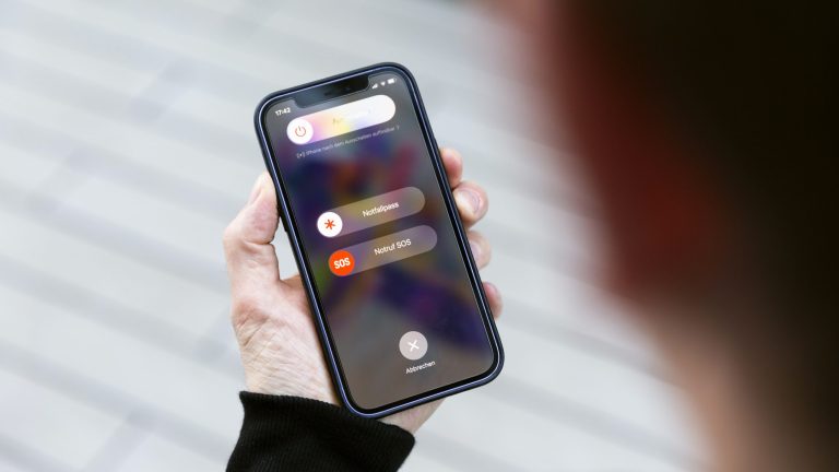 iPhone Gesten Eine Person hält ein iPhone 12 in der Hand und betätigt die Seitentaste sowie eine der Lautstärke-Tasten. Auf dem Display sind die Optionen zu sehen, dass Gerät auszuschalten, ein, den Notfallpass zu aktivieren oder einen Notruf abzusetzen.
