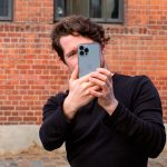 Eine Person fotografiert mit einem iPhone 13 Pro Max vor einer Steinwand.