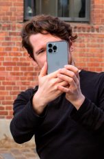 Eine Person fotografiert mit einem iPhone 13 Pro Max vor einer Steinwand.