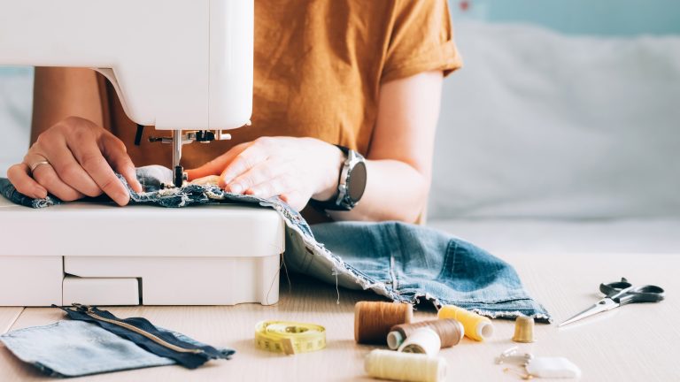 Nähmaschine Anfänger Eine Person sitzt an einer Nähmaschine. Neben ihr liegen einige Fäden, eine Schere und mehr.