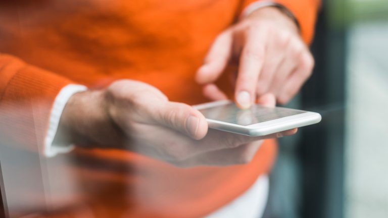 Eine Person in orangefarbenem Sweater tippt auf einem Smartphone.