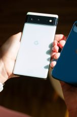 Zwei Hände halten jeweils ein Smartphone: Einmal ein weißes Google Phone und einmal ein dunkelblaues iPhone.