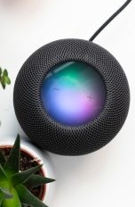 Ein schwarzer Apple HomePod steht neben zwei Pflanzen auf einem weißen Tisch.