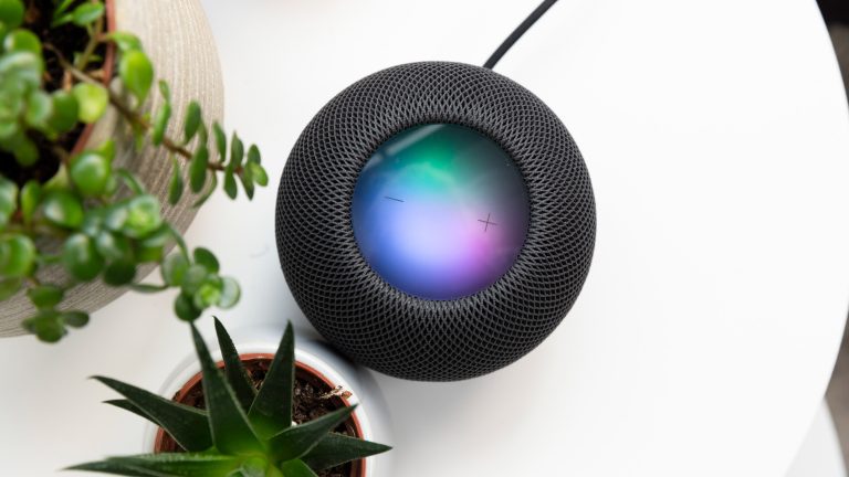 Ein schwarzer Apple HomePod steht neben zwei Pflanzen auf einem weißen Tisch.