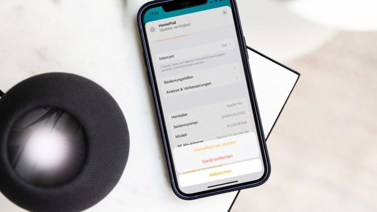 HomePod Mini zurücksetzen Ein schwarzer HomePod mini und ein iPhone 12 liegen auf einem Marmortisch.