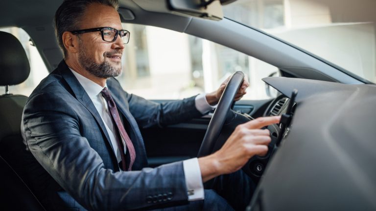 Eine Person sitzt am Steuer eines Autos und tippt auf einem Smartphone, das an einem L&uuml;ftungsgitter angebracht ist.