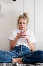 Eine Person sitzt im Schneidersitz auf einem Bett und schaut auf ein Smartphone, das sie in den Händen hält.