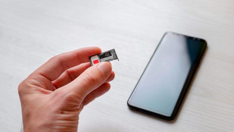WhatsApp Smartphone Wechsel Eine Hand hält einen SlM-Karten-Einschub eines Smartphones ins Bild. In den Einschub sind eine SIM-Karte und eine microSD-Karte eingelegt.