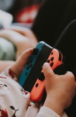 Ein Kind hält zwei Joy-Cons von Nintendo in ihrer Halterung in der Hand.