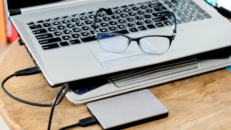 Windows Speicherplatz freigeben Auf einem Tisch steht ein Laptop mit externer Festplatte, auf ihm liegt eine Brille.