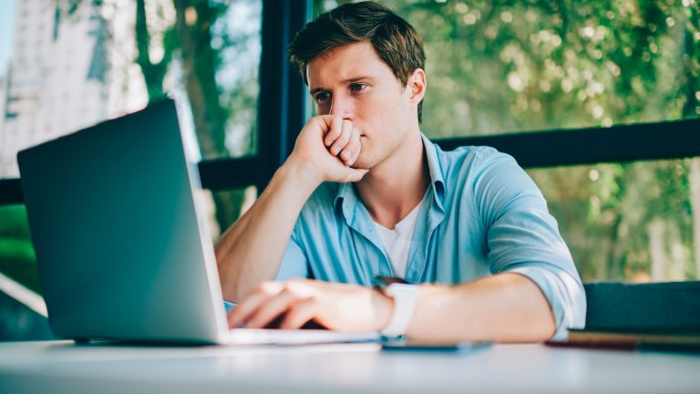 Eine Person sitzt vor einem Laptop und blickt angestrengt auf den Bildschirm.