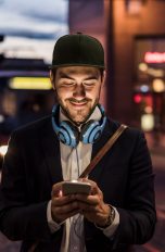Eine Person ist am Abend in der Stadt unterwegs und schaut auf ihr Smartphone.