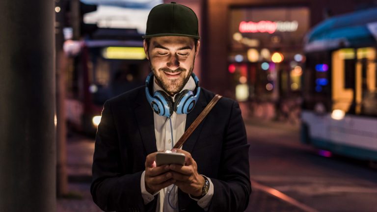 Eine Person ist am Abend in der Stadt unterwegs und schaut auf ihr Smartphone.