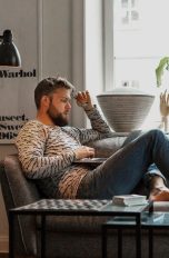 Eine Person sitzt mit einem Laptop auf den Knien auf einem Sofa.