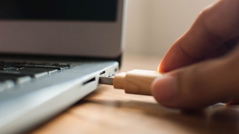 Chrome OS Flex Eine Hand steckt einen USB-Stick in den Anschluß eines Laptops.