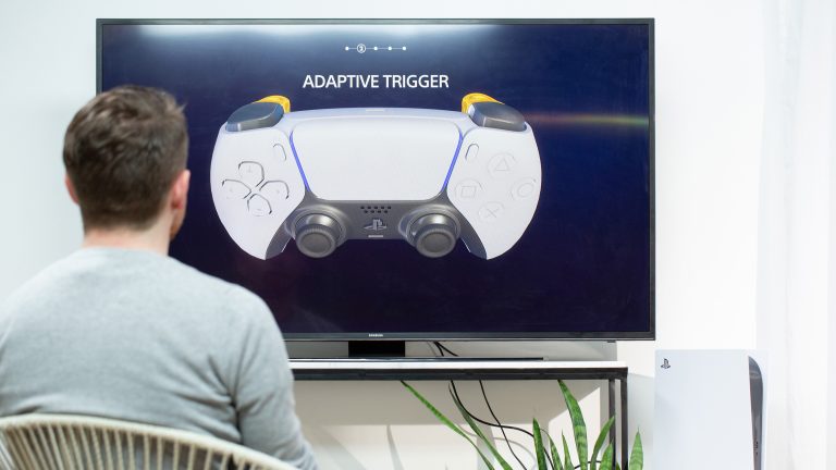 Playstation 5 Dual Sense Eine Person sitzt vor einem Fernseher und schaut sich die Erklärung zu den adaptiven Triggern im DualSense an.