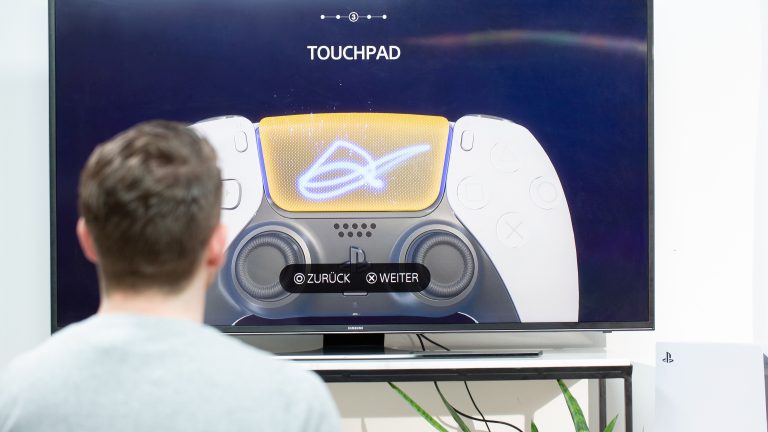 Playstation 5 Dual Sense Eine Person sitzt vor einem Fernseher und schaut sich den Erklärfilm zum Touchpad im DualSense-Controller an.