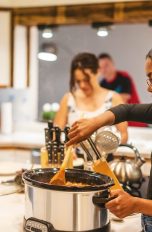 Slow Cooker Eine Person steht vor einem Slow-Cooker-Kochtopf und rührt darin mit einem Holzlöffel.